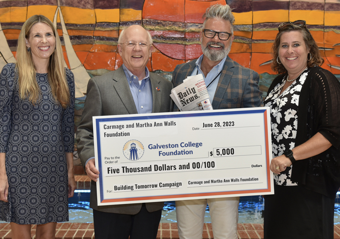 Four people smile and pose with a large check for donation.