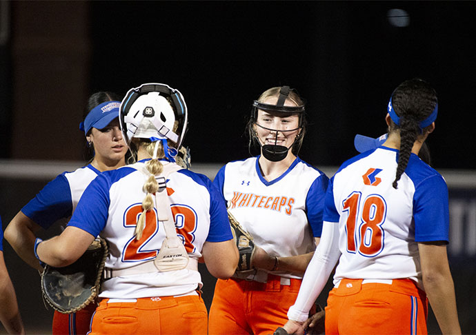 Softball players huddle on field together during game