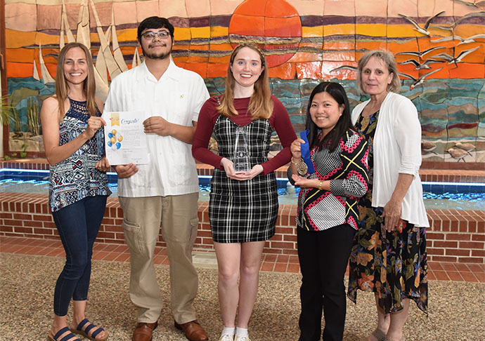 5 people stand holding awards in front sunset mural