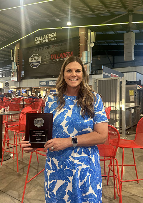 Softball coach stands with award