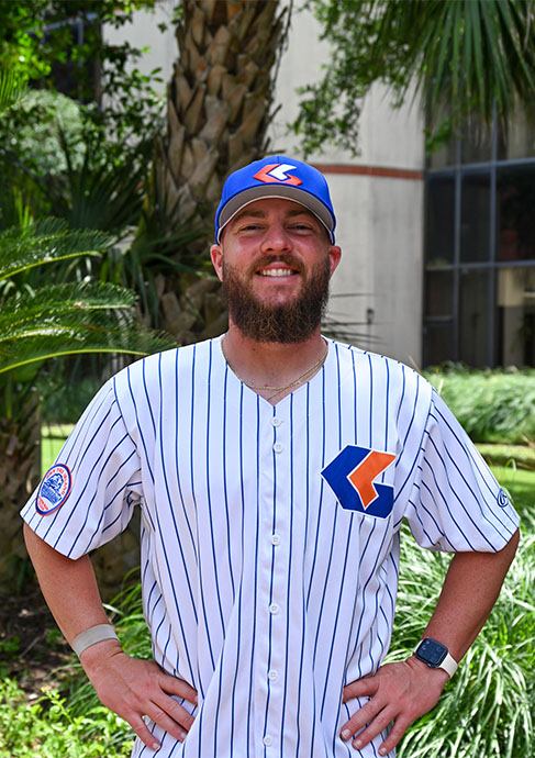 Baseball coach stands outside among greenery 