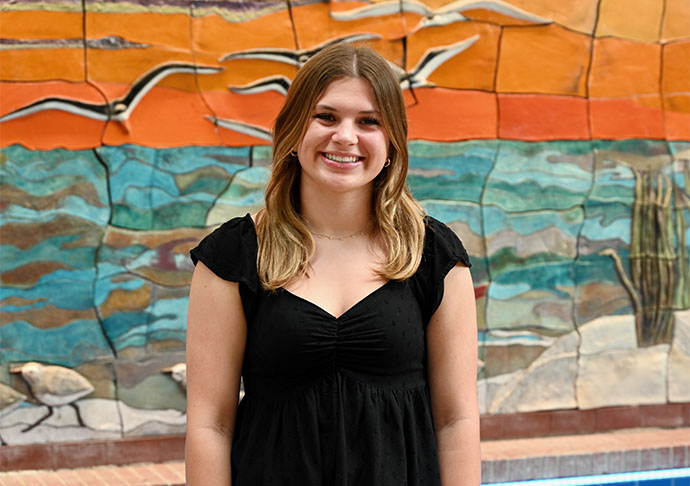 Student poses in front of sunset mural