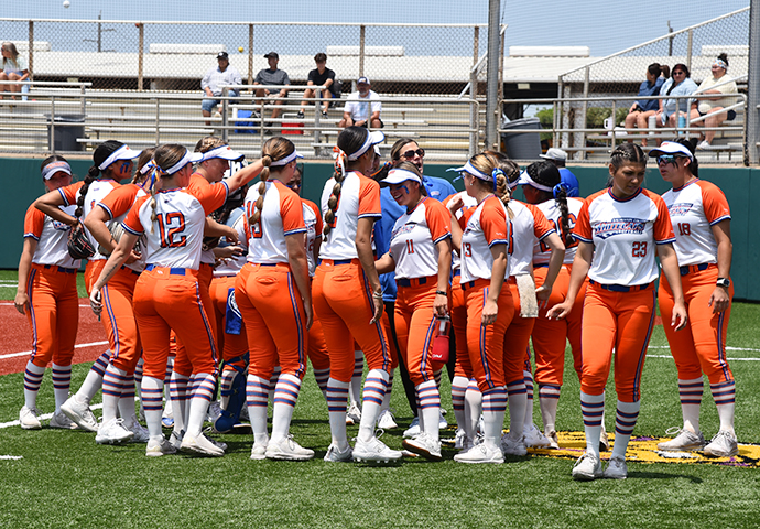 Softball players gather with coaches on the field.