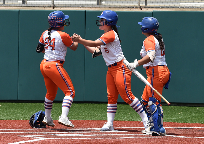 Three softball players celebrate on base.