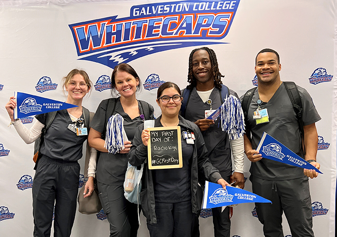 Students in scrubs pose with pennant flags and pom poms for Welcome Week. 