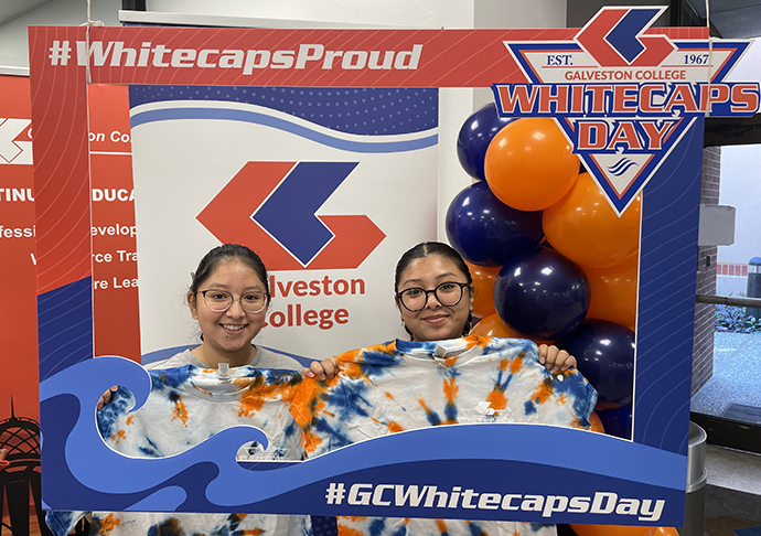 Two people hold up their orange and blue tie-dyed shirts in a photo booth frame.